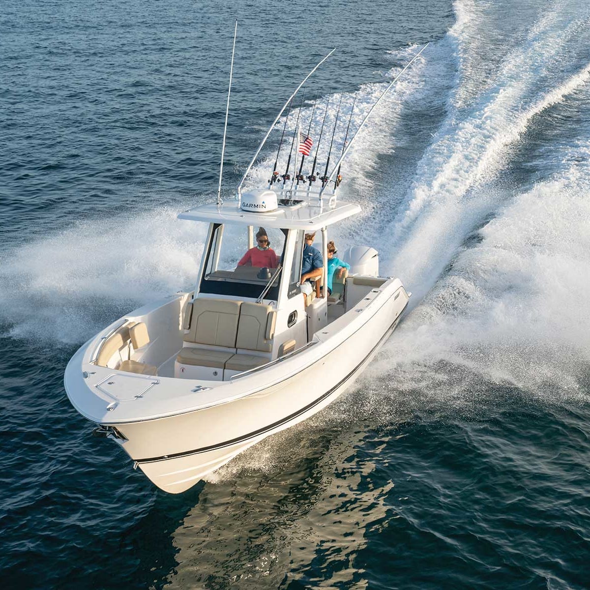 Boat speeding across water with three people, fishing rods, and white hull.