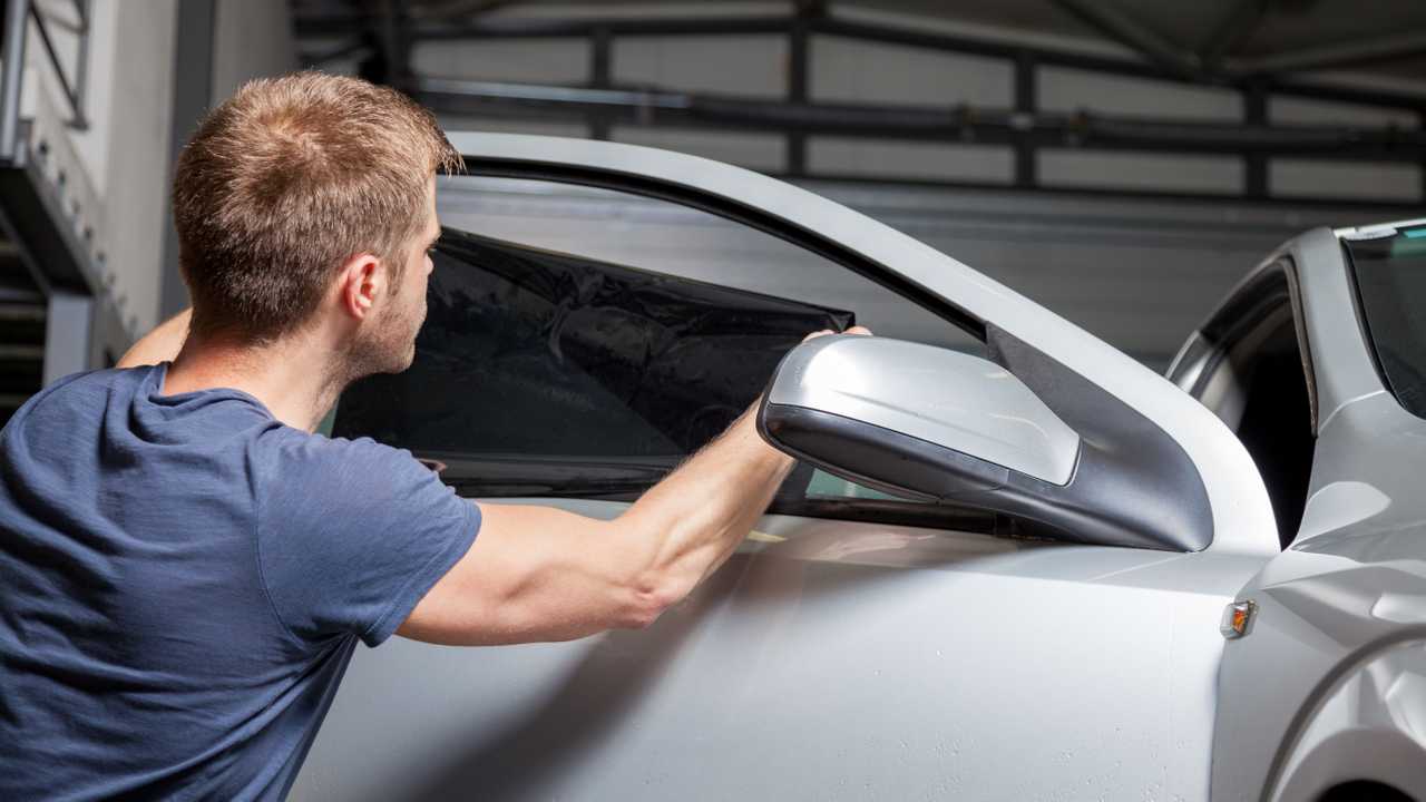 Man applying tinted film to a car window in a garage.