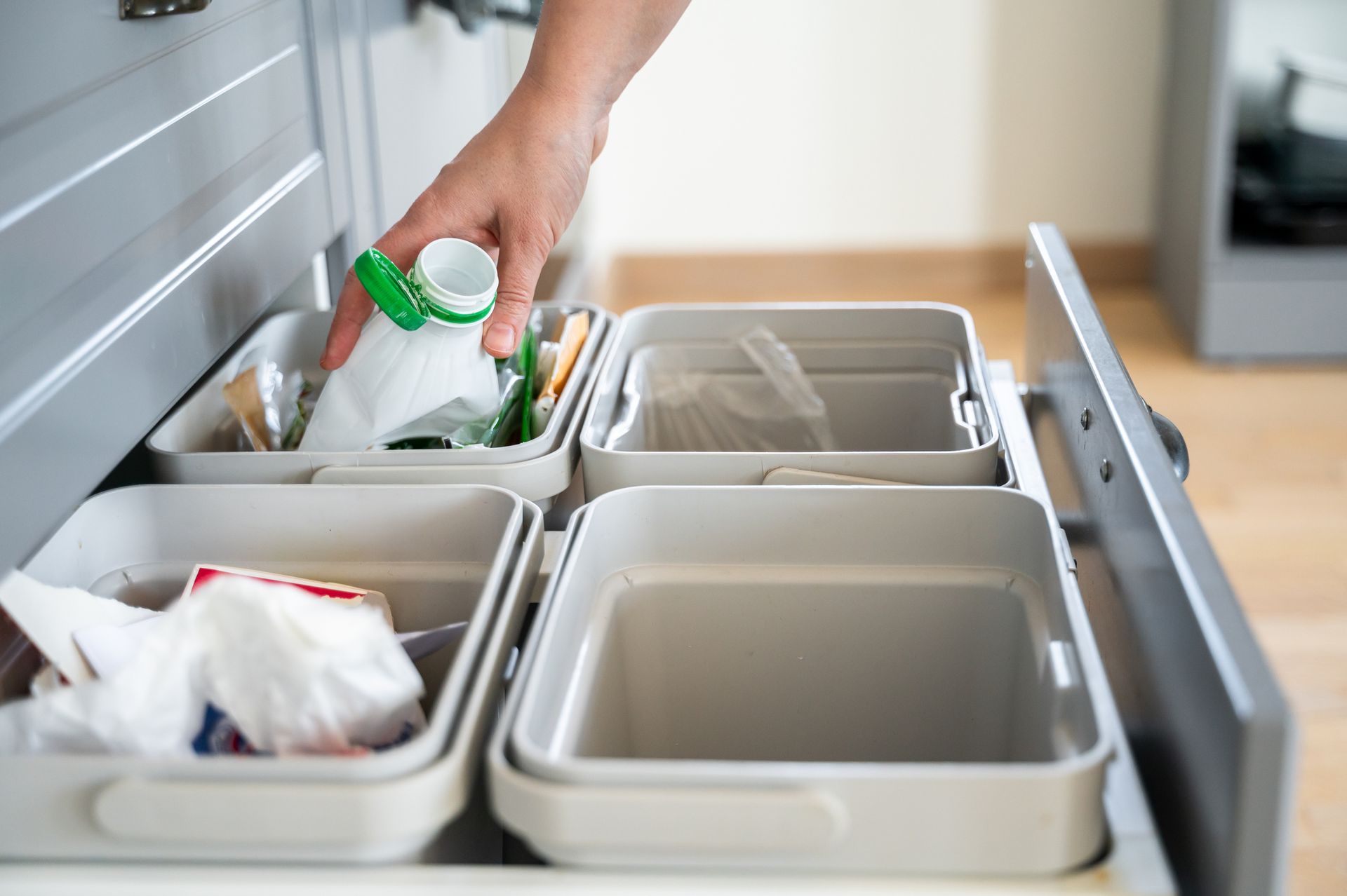 A person is putting a bottle of milk into a trash can in a kitchen. A person is putting a bottle of milk into a trash can in a kitchen.