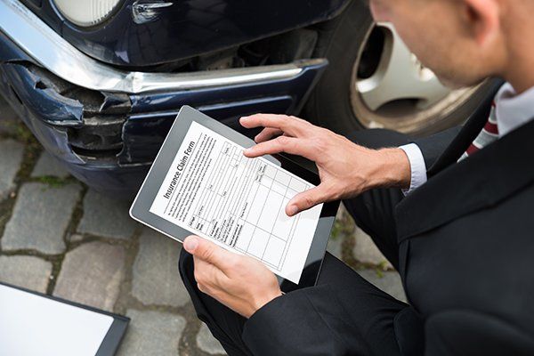 Man Holding Digital Tablet Examining Damaged Car — Chicago, IL — Illinois Insurance Center Inc