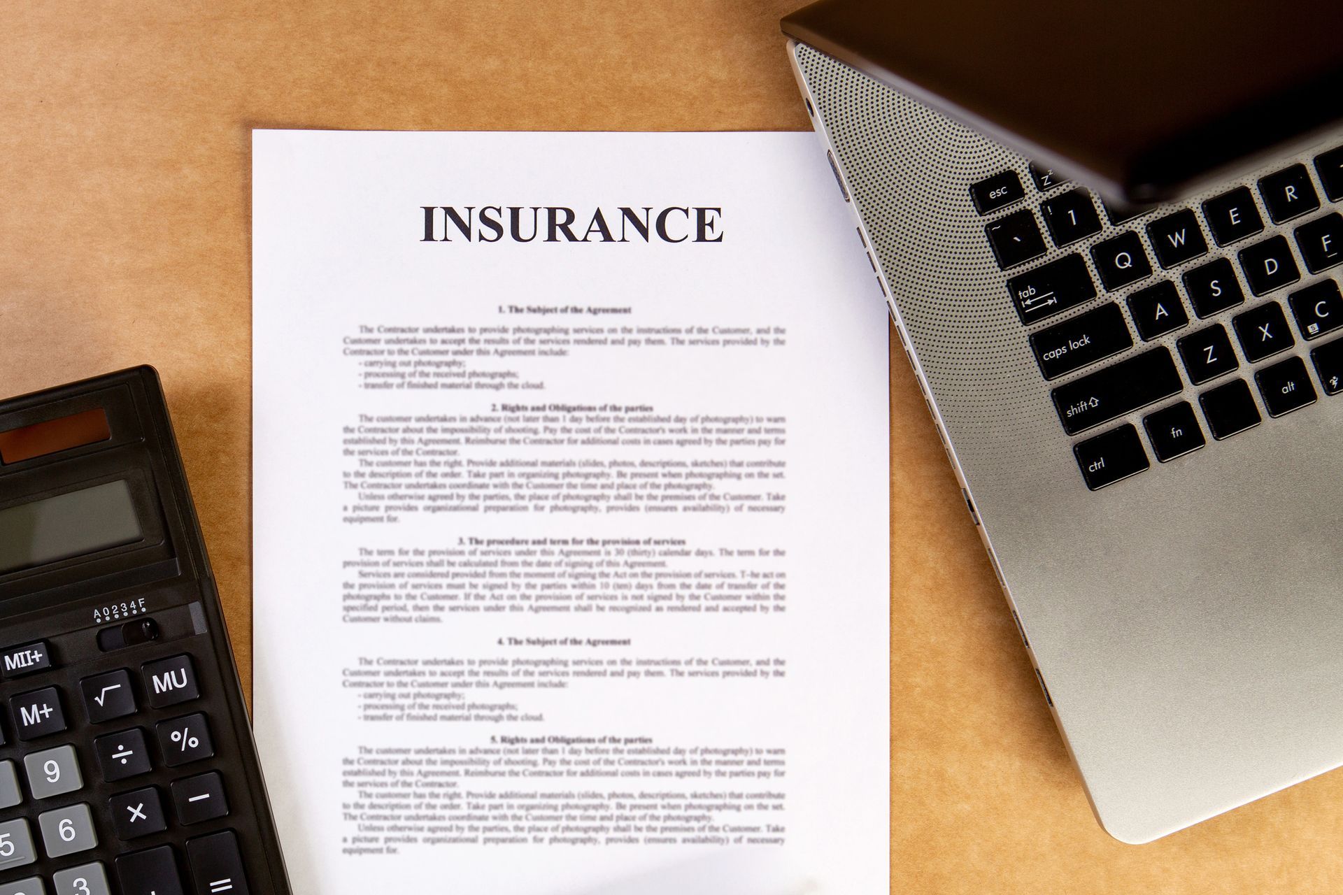 Insurance document with a calculator and laptop on a wooden surface.