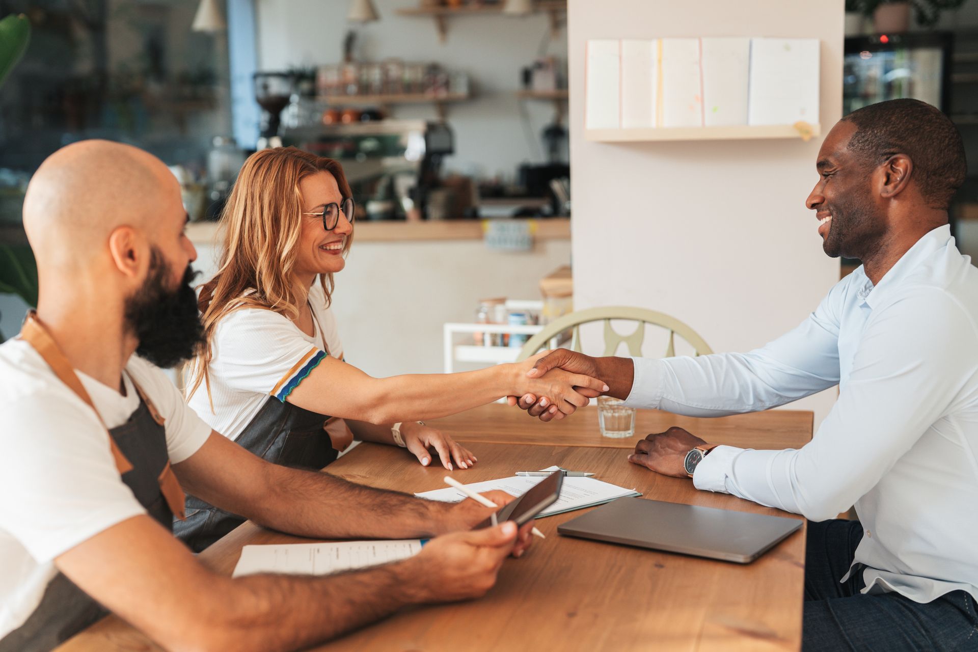 Coffee shop owners are shaking hands with an insurance agent.