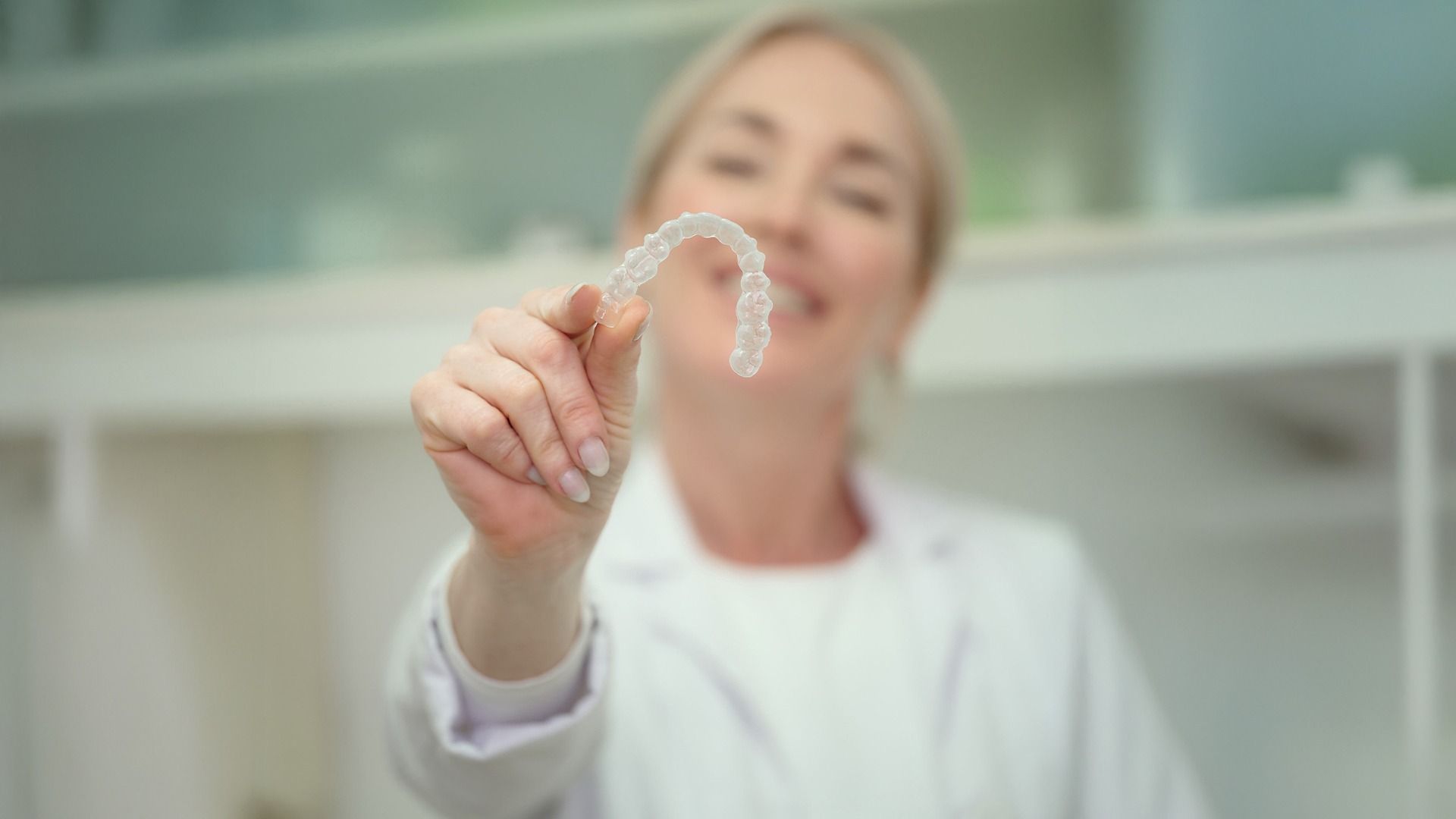 Mujer sosteniendo un alineador dental transparente frente a la cámara en una clínica luminosa.