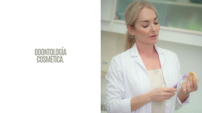 Promoción de odontología cosmética con un dentista con bata blanca sosteniendo un modelo dental en una clínica luminosa.