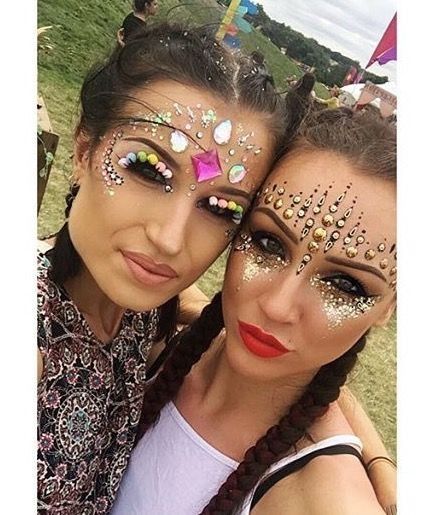 Dos mujeres en un festival, con el rostro adornado con purpurina y gemas. Sonríen, con el cabello trenzado.