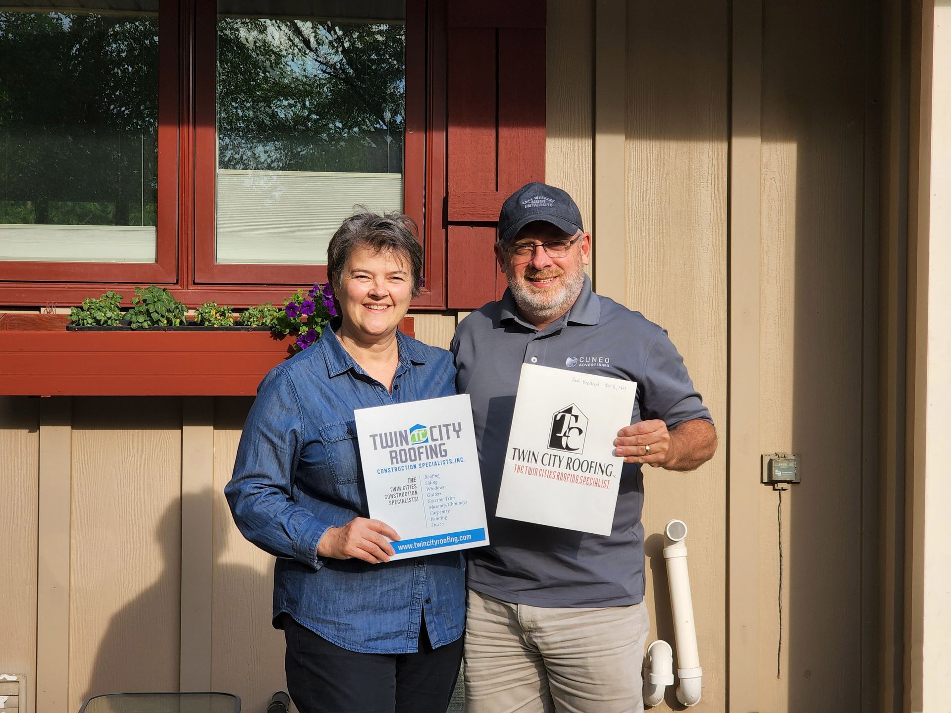 A man and a woman are standing in front of a house holding signs.