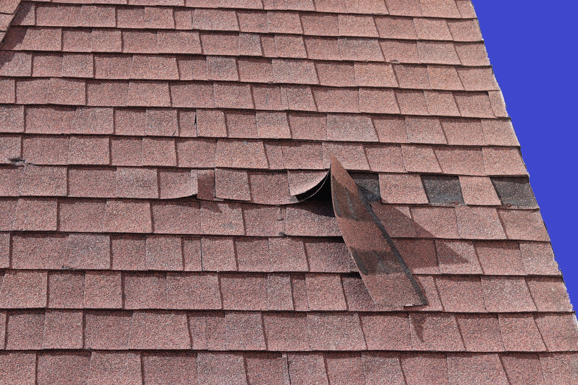 Storm damaged red shingles on a residential roof in Minneapolis Minnesota that needs repairs 