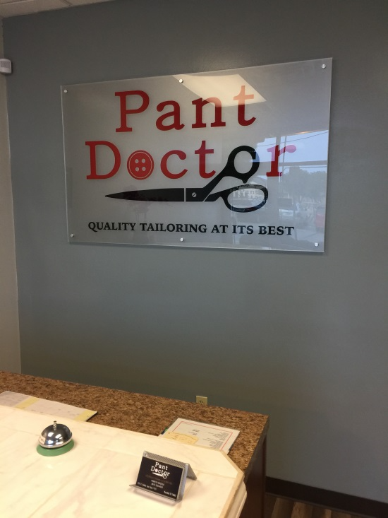 Tailoring shop sign reading “Pant Doctor” on a gray wall above a counter