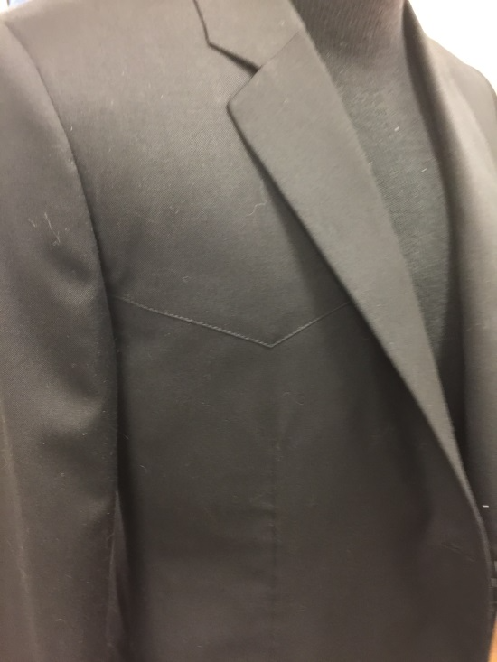 Close-up of a person wearing a dark gray suit jacket over a black shirt.