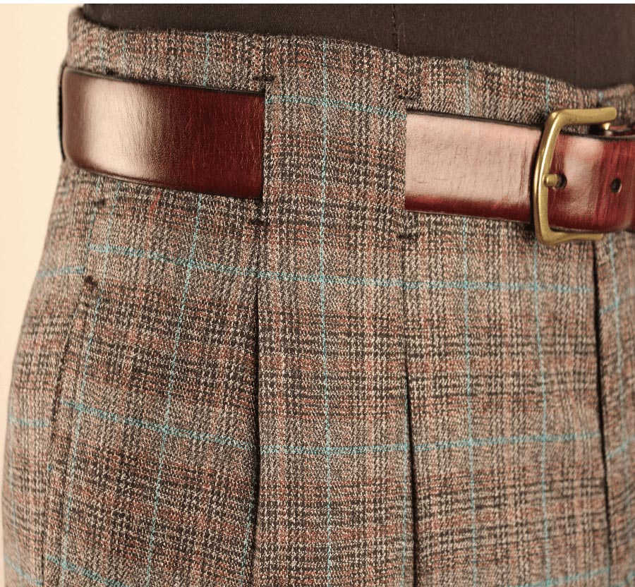 Close-up of brown plaid trousers with a belt and gold buckle at the waist.