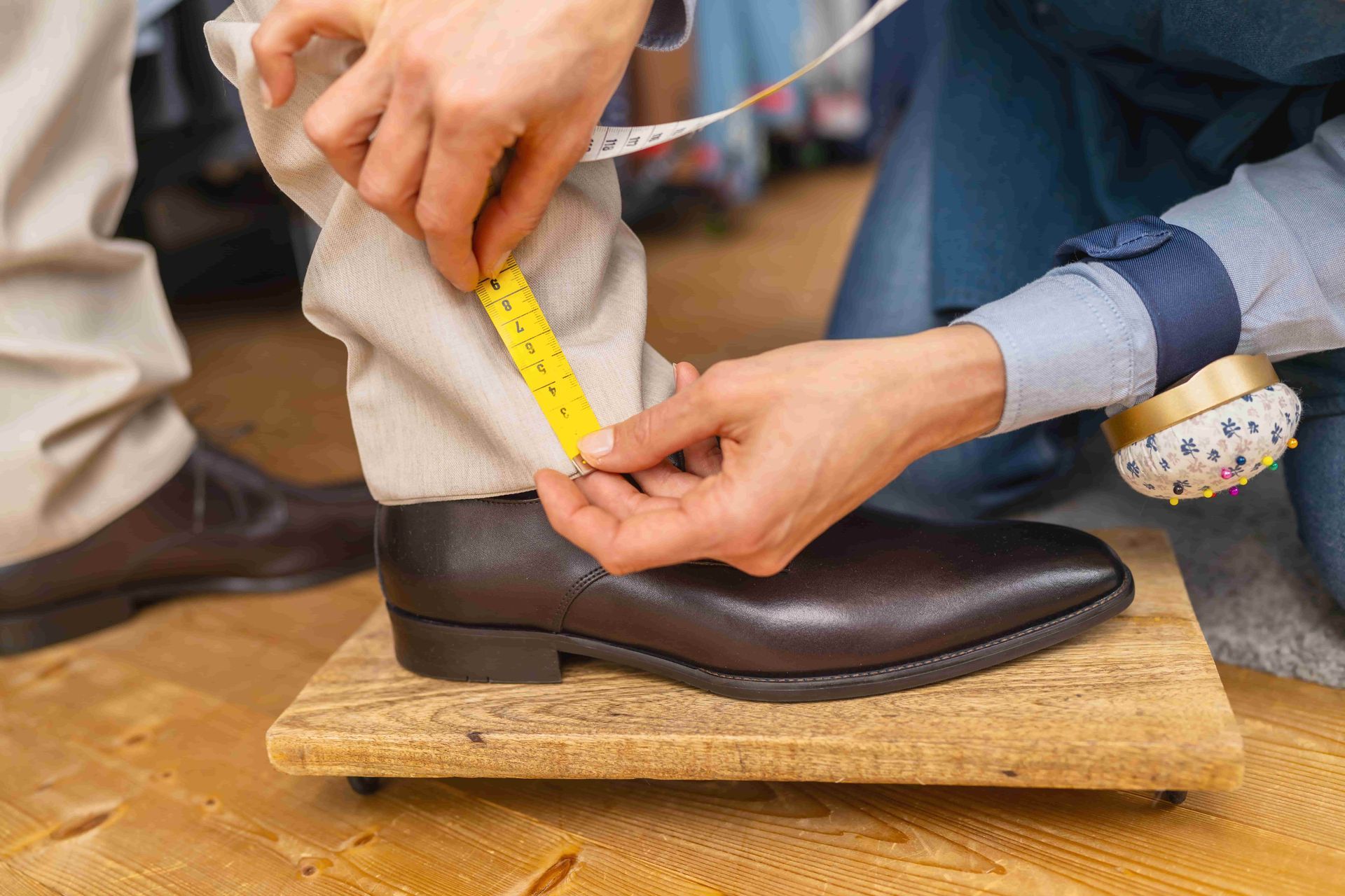 Hands measuring a brown leather boot with a yellow tape measure on a wooden block.