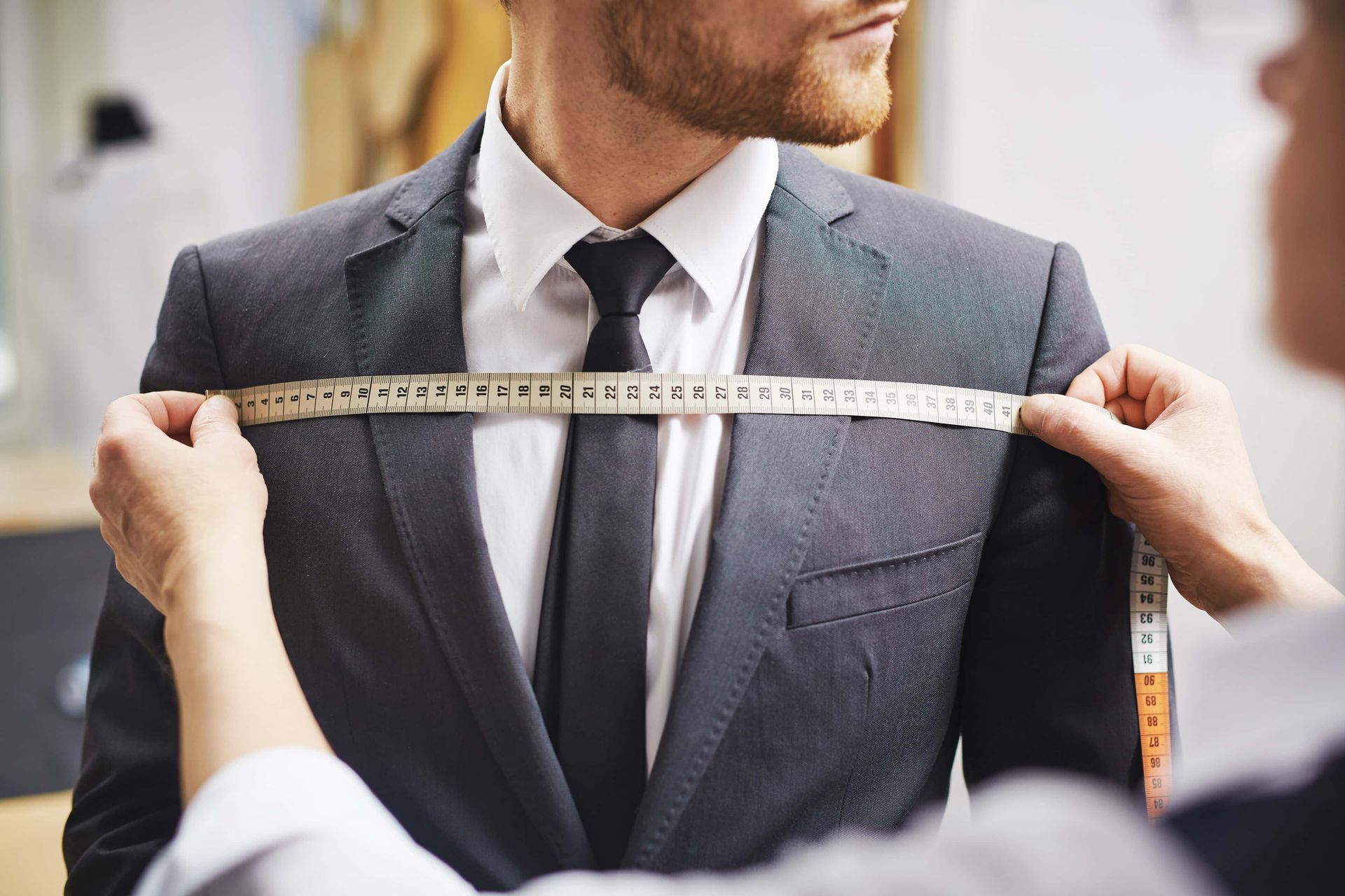 Tailor measuring a man’s suit jacket with a tape measure