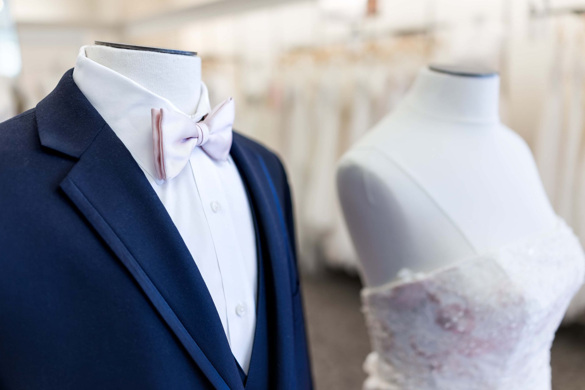 Mannequin in navy suit with pink bow tie beside bridal dress mannequin in a boutique