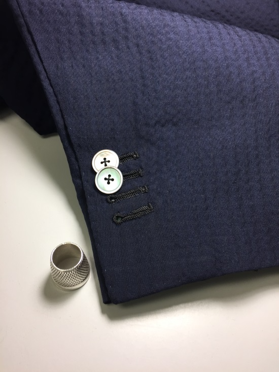 Dark blue blazer sleeve with two buttons beside a silver thimble on a light surface