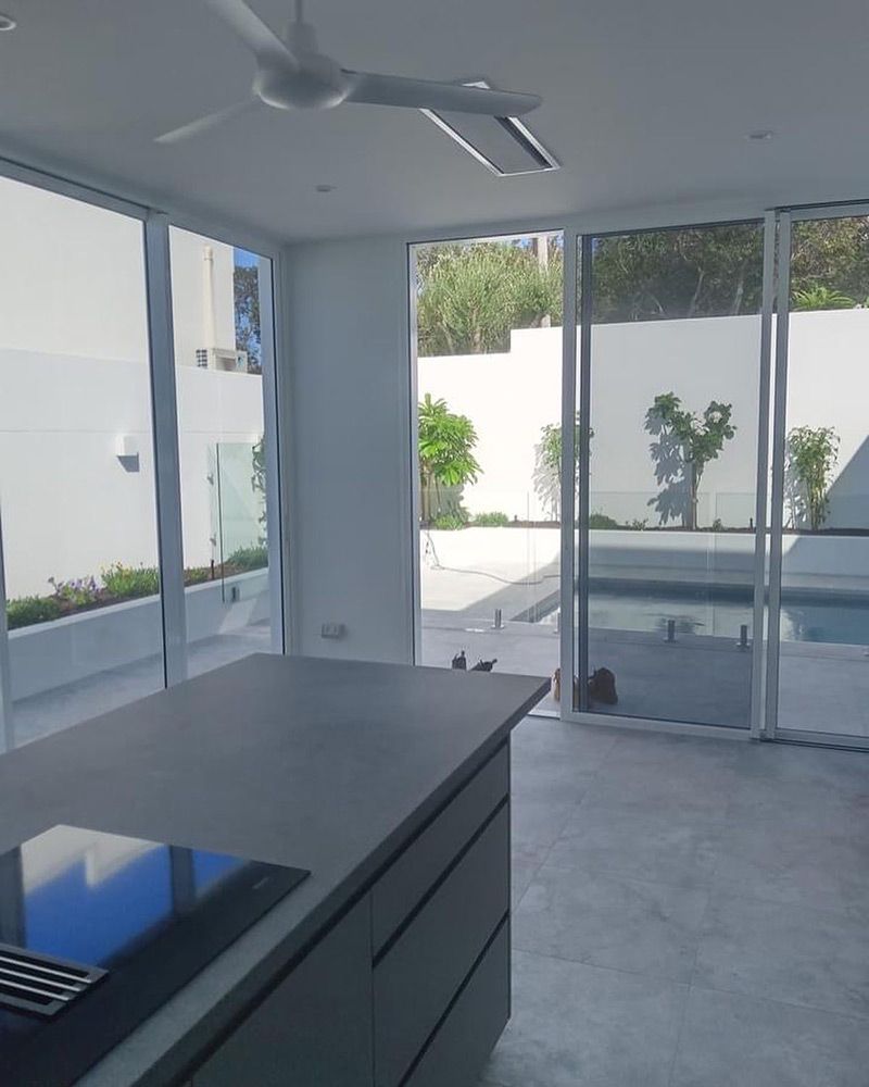 Modern Kitchen With Grey Island and Large Windows Overlooking a Pool — Architectural Glass Solutions QLD in Cooroy, QLD