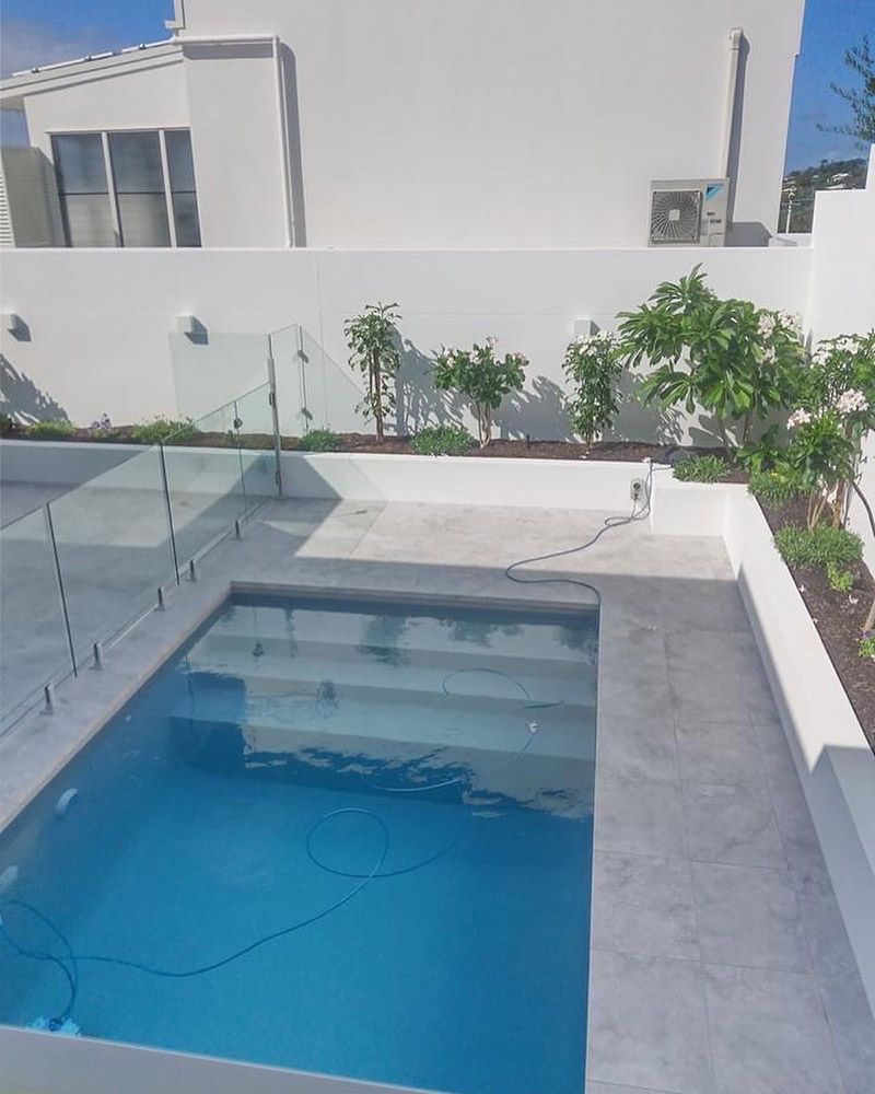 A Rectangular Swimming Pool is Surrounded by a Tiled Patio. Glass Fencing — Architectural Glass Solutions QLD in Cooroy, QLD
