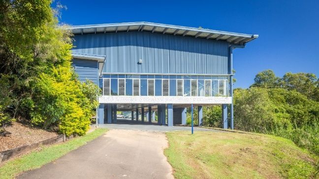 A Large Blue Building With a Driveway Leading to It is Surrounded by Trees — Architectural Glass Solutions QLD in Cooroy, QLD