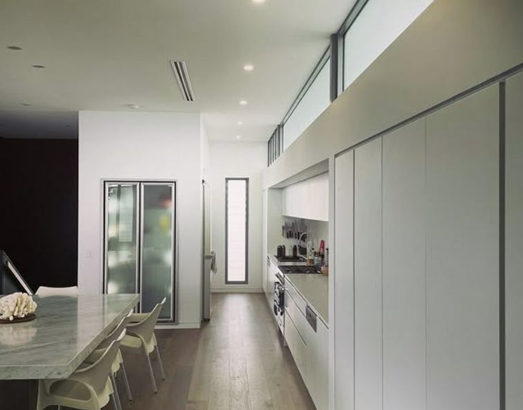 Modern White Kitchen With Long Counters, Cabinets & Island With Chairs — Architectural Glass Solutions QLD in Cooroy, QLD