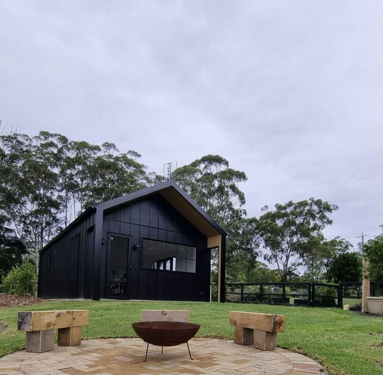 A Modern Black Cabin With a Fire Pit and Seating on a Grassy Area — Architectural Glass Solutions QLD in Cooroy, QLD
