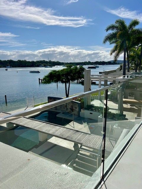 A balcony overlooking a body of water with palm trees — Architectural Glass Solutions QLD in Cooroy, QLD