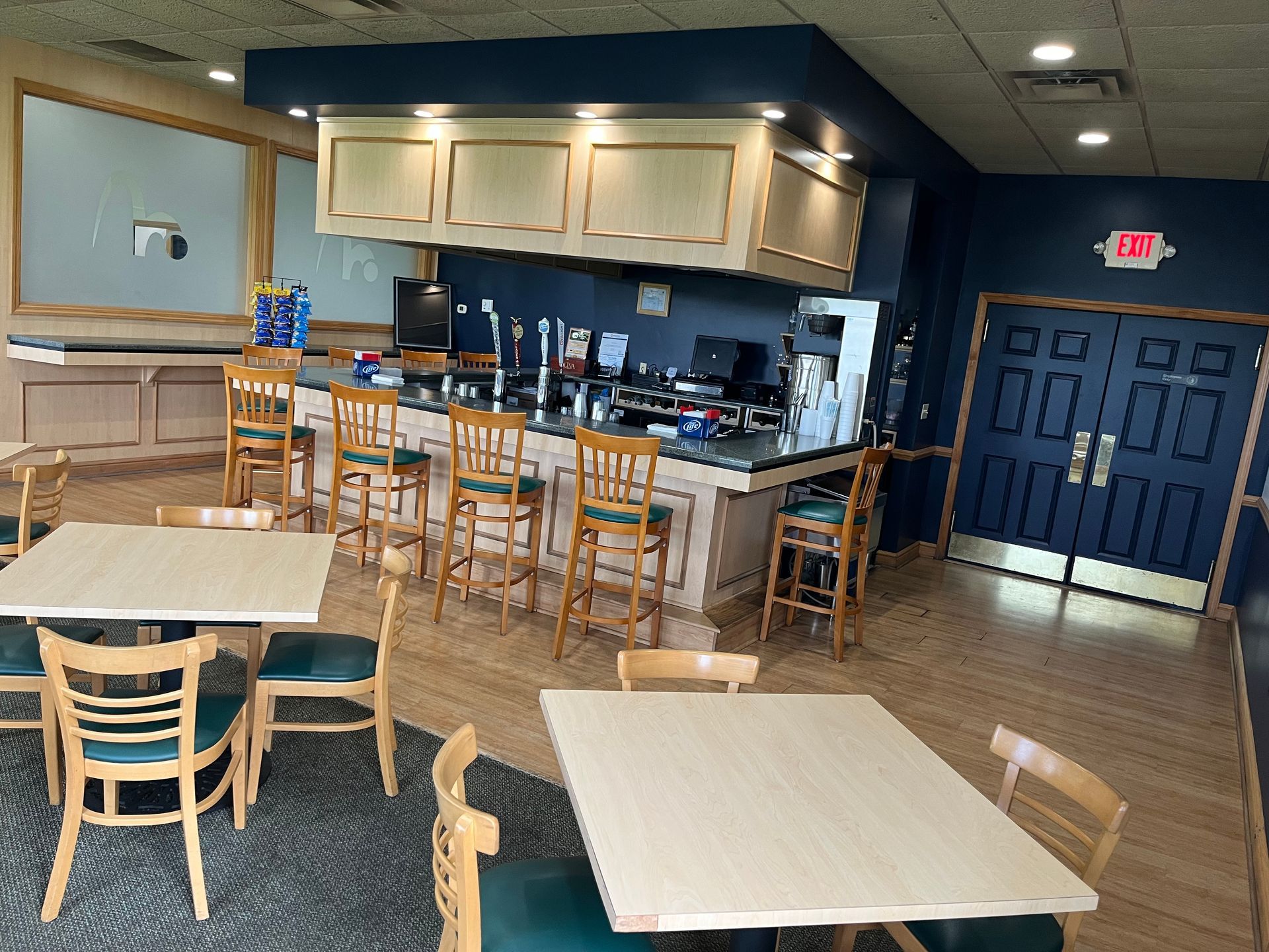 A bar with stools, tables, and chairs in a room. The room has blue walls, and a set of double doors.