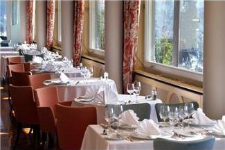 Restaurant dining area with tables set for service, beside large windows with red patterned curtains.
