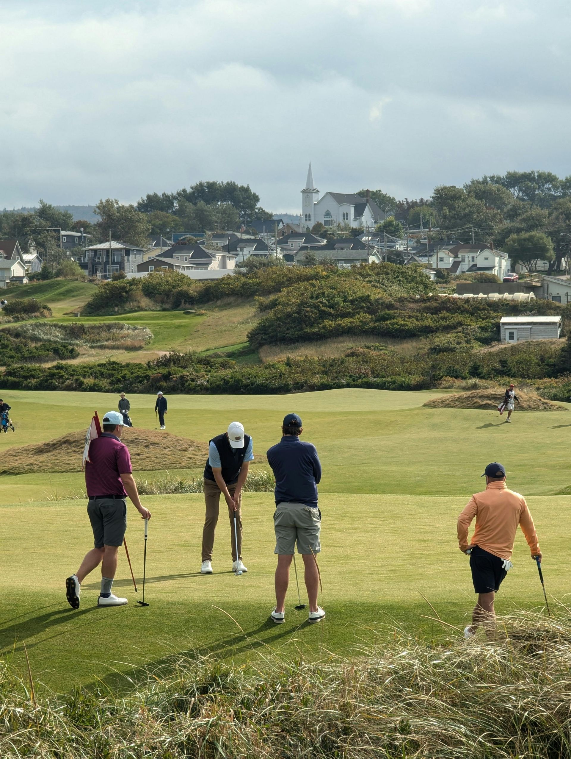 Golfers on a green with town and church in the background on a cloudy day.