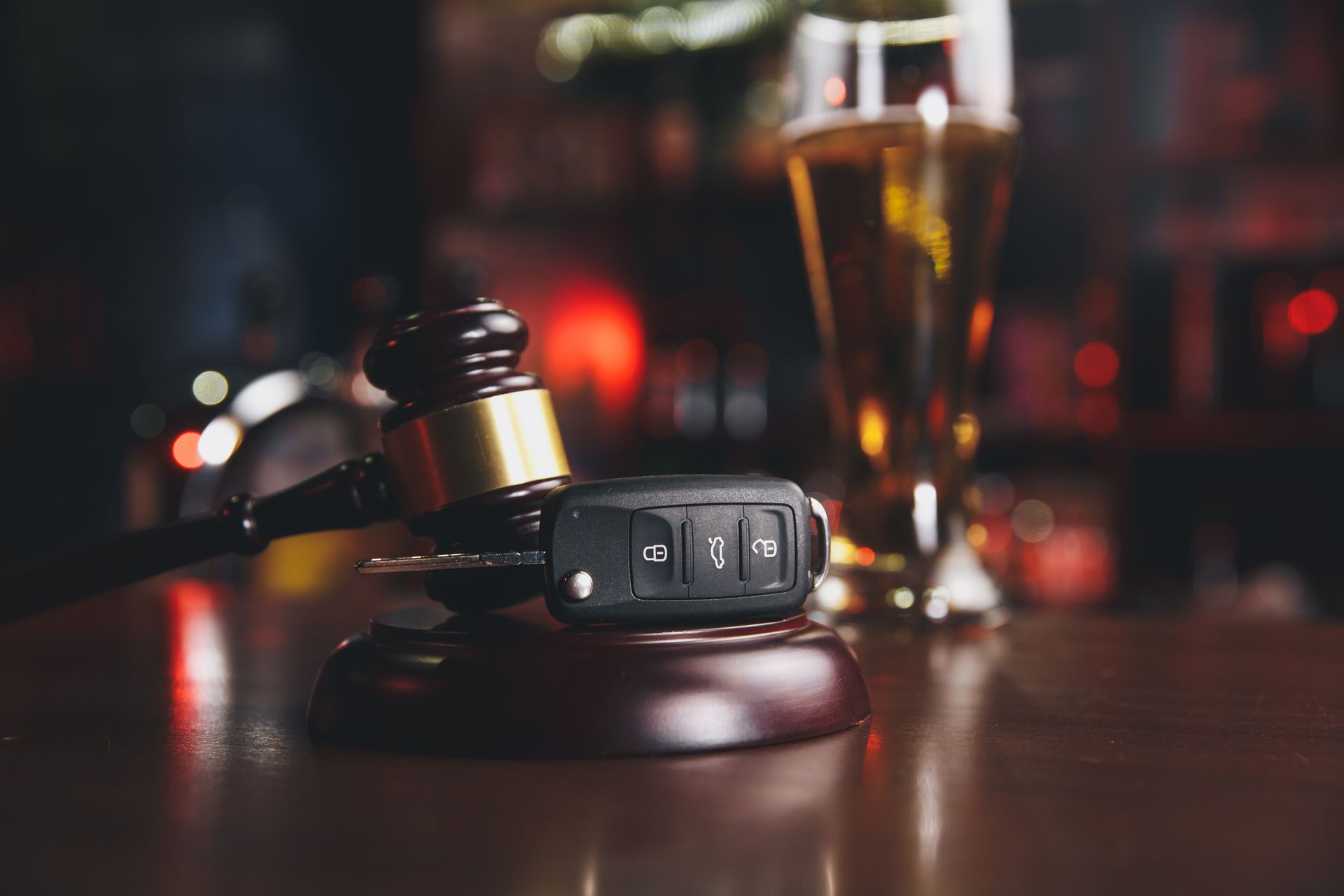 A car key is sitting on top of a wooden gavel next to a glass of beer.