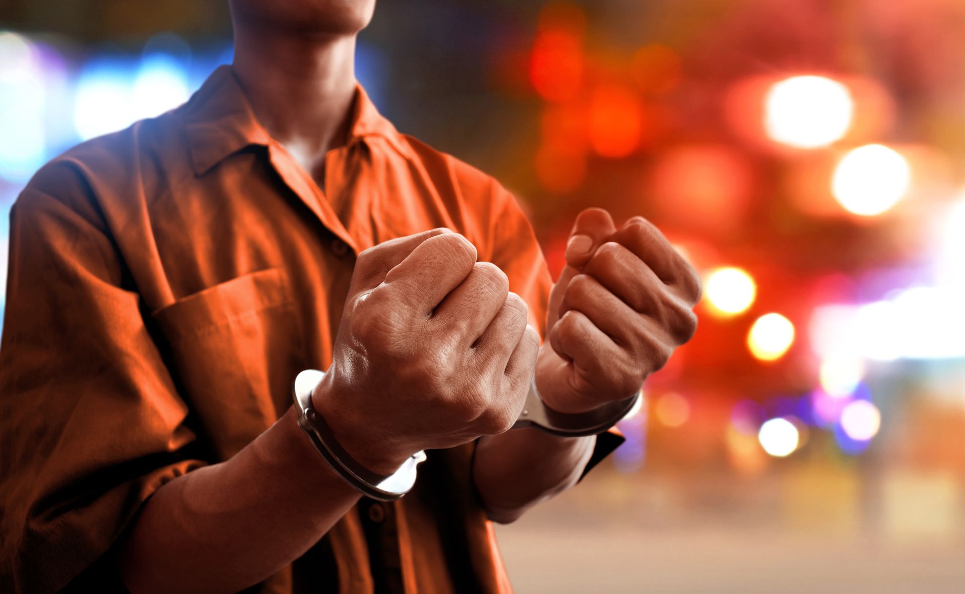 A man wearing handcuffs is standing in front of a blurry background.