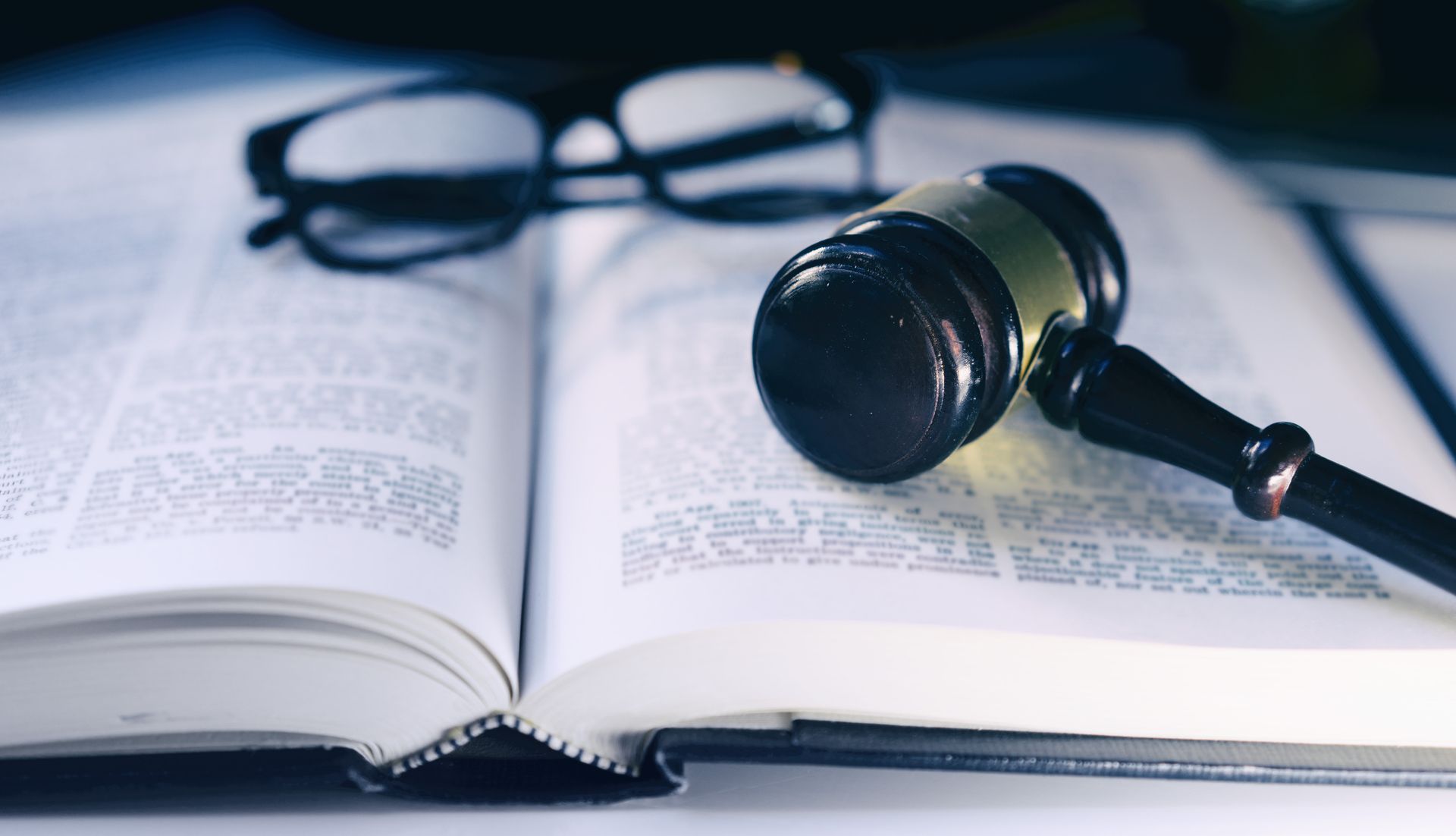 A judge 's gavel is sitting on top of an open book next to a pair of glasses.