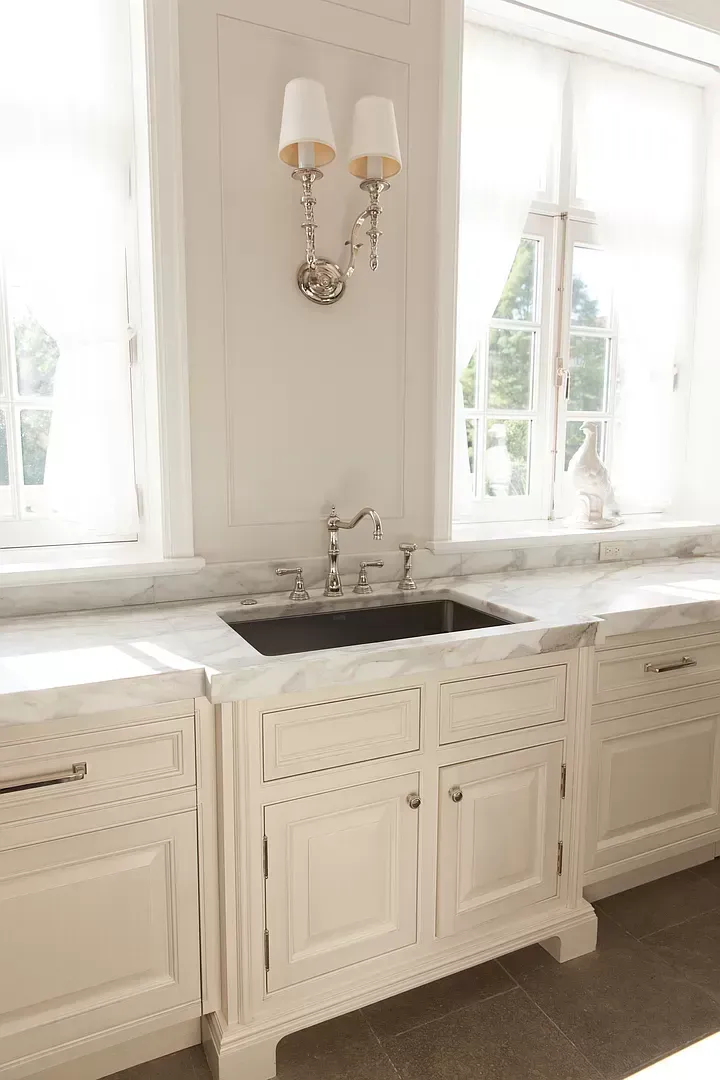 A kitchen with white cabinets , a sink , and a window.