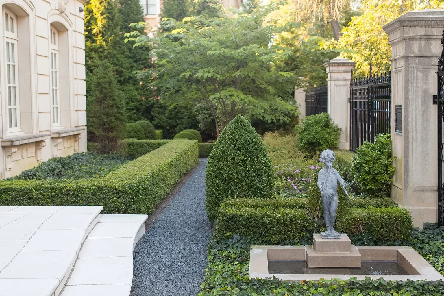 A statue of a boy standing next to a fountain in a garden.