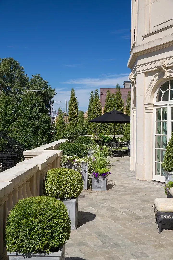 A balcony with a lot of plants and a black umbrella on a sunny day.