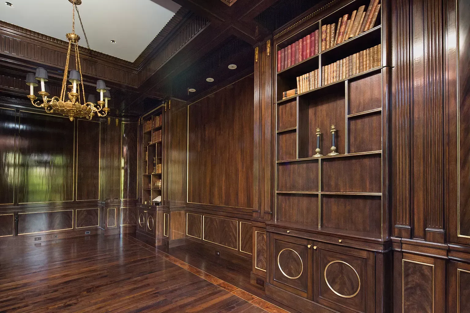 A library with wooden walls and shelves and a chandelier hanging from the ceiling.