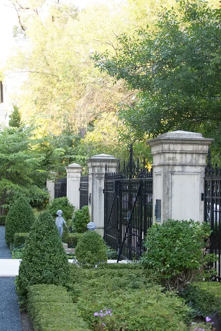 There is a gate in the middle of a garden surrounded by bushes and trees.