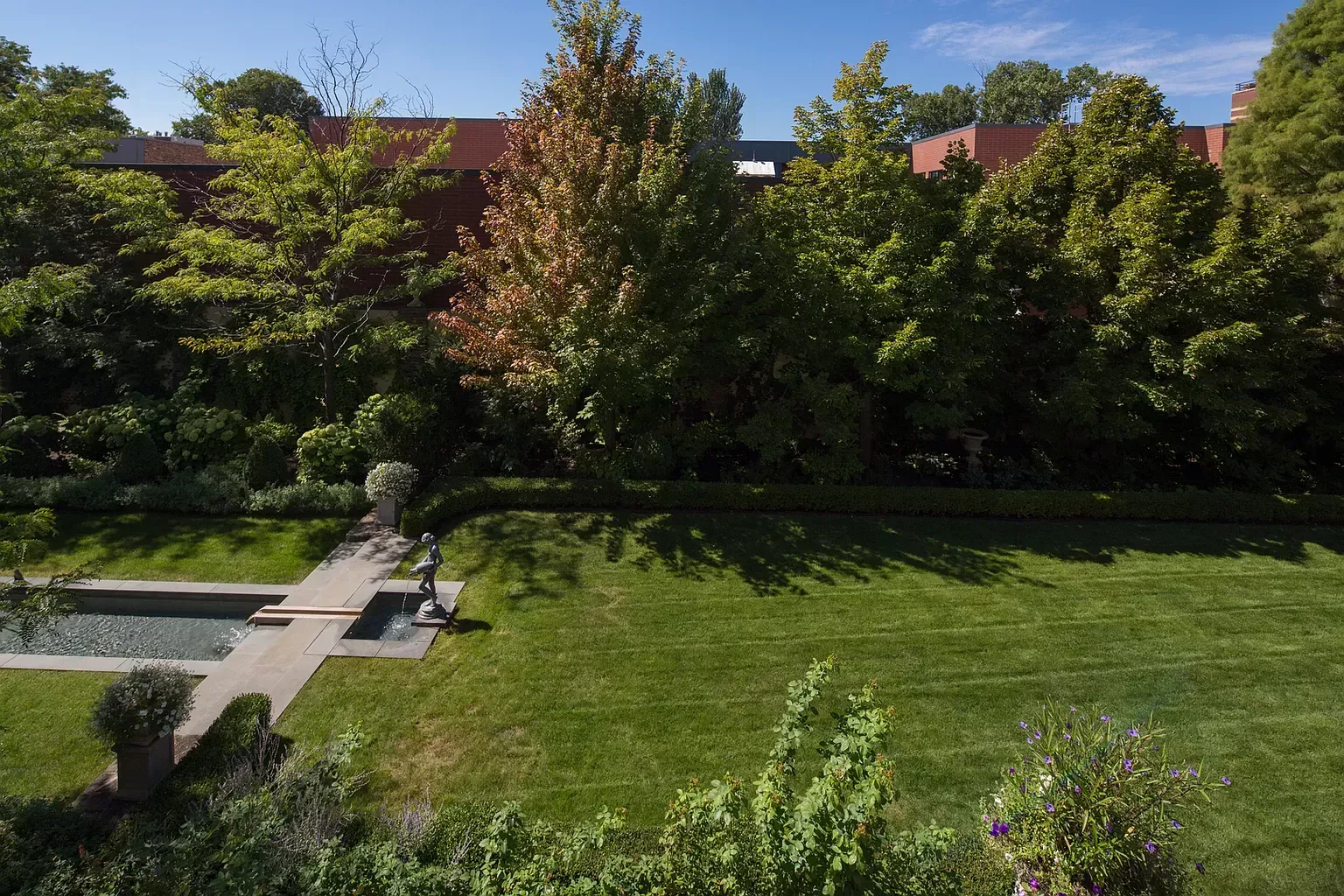 An aerial view of a large lush green lawn with a swimming pool surrounded by trees.