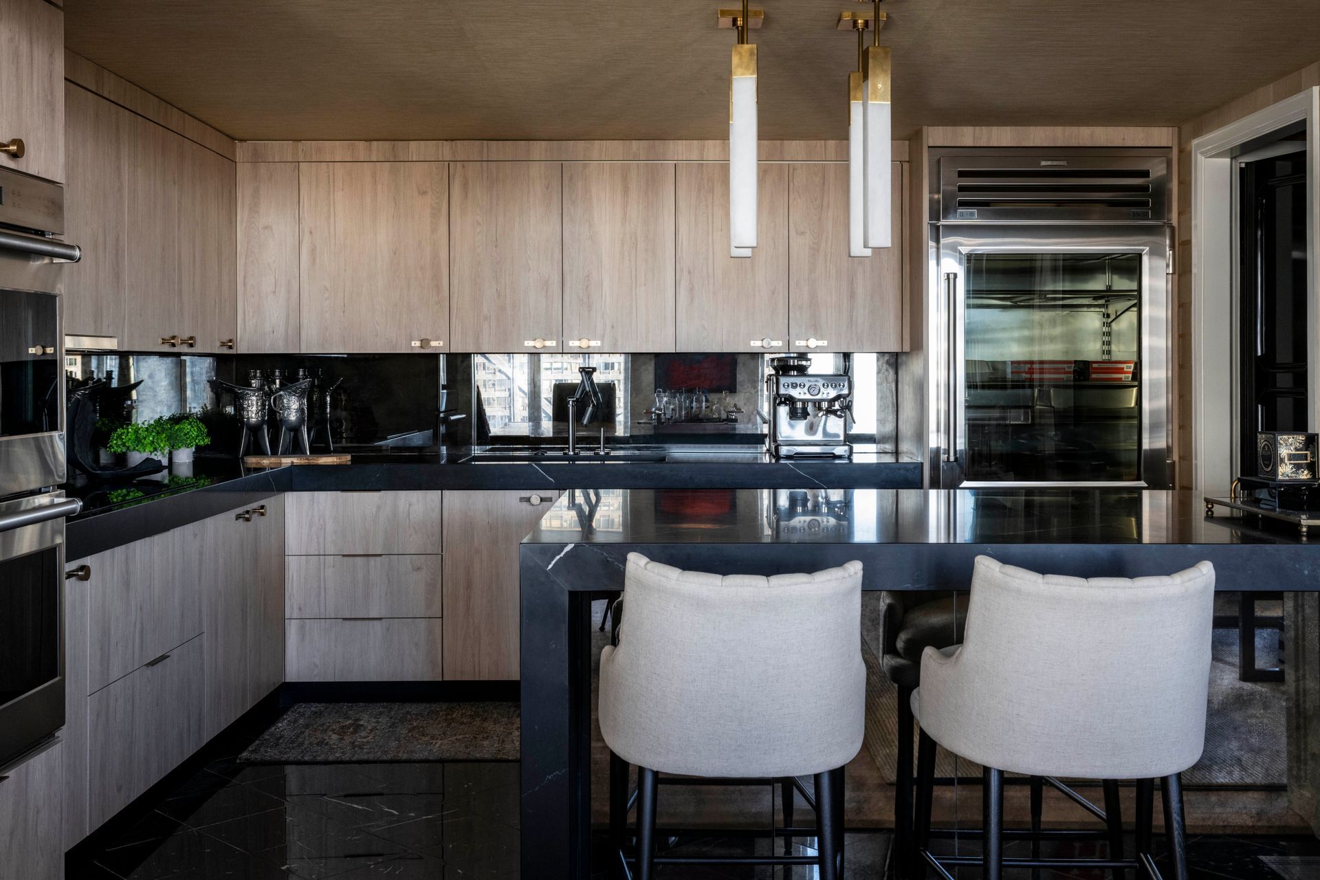 A kitchen with wooden cabinets , black counter tops , stainless steel appliances , a refrigerator and a bar.