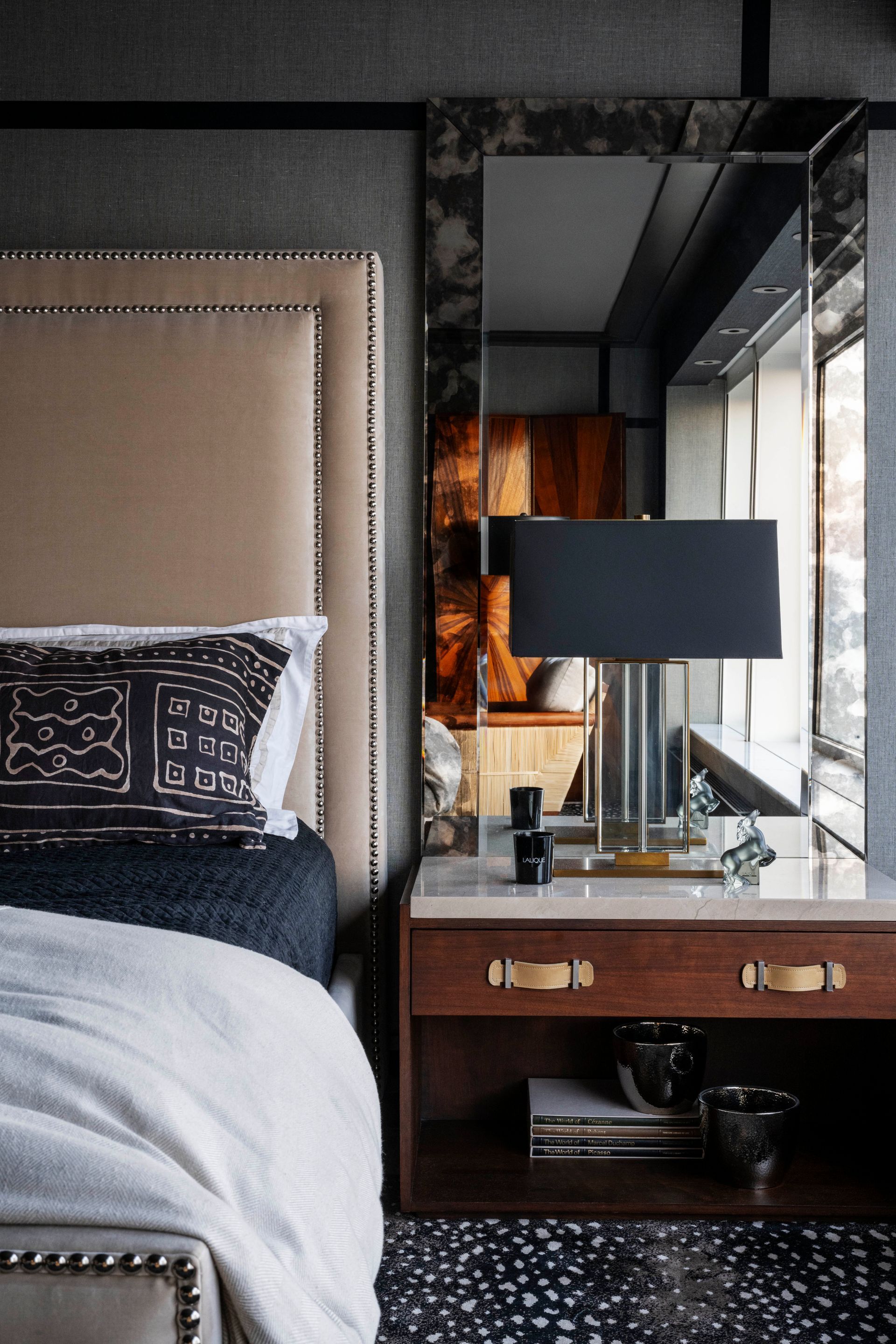 A bedroom with a bed , nightstand , lamp and mirror