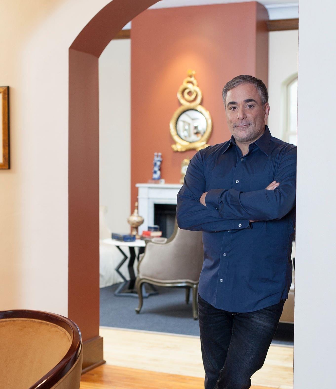 A man in a blue shirt is standing in a room with his arms crossed