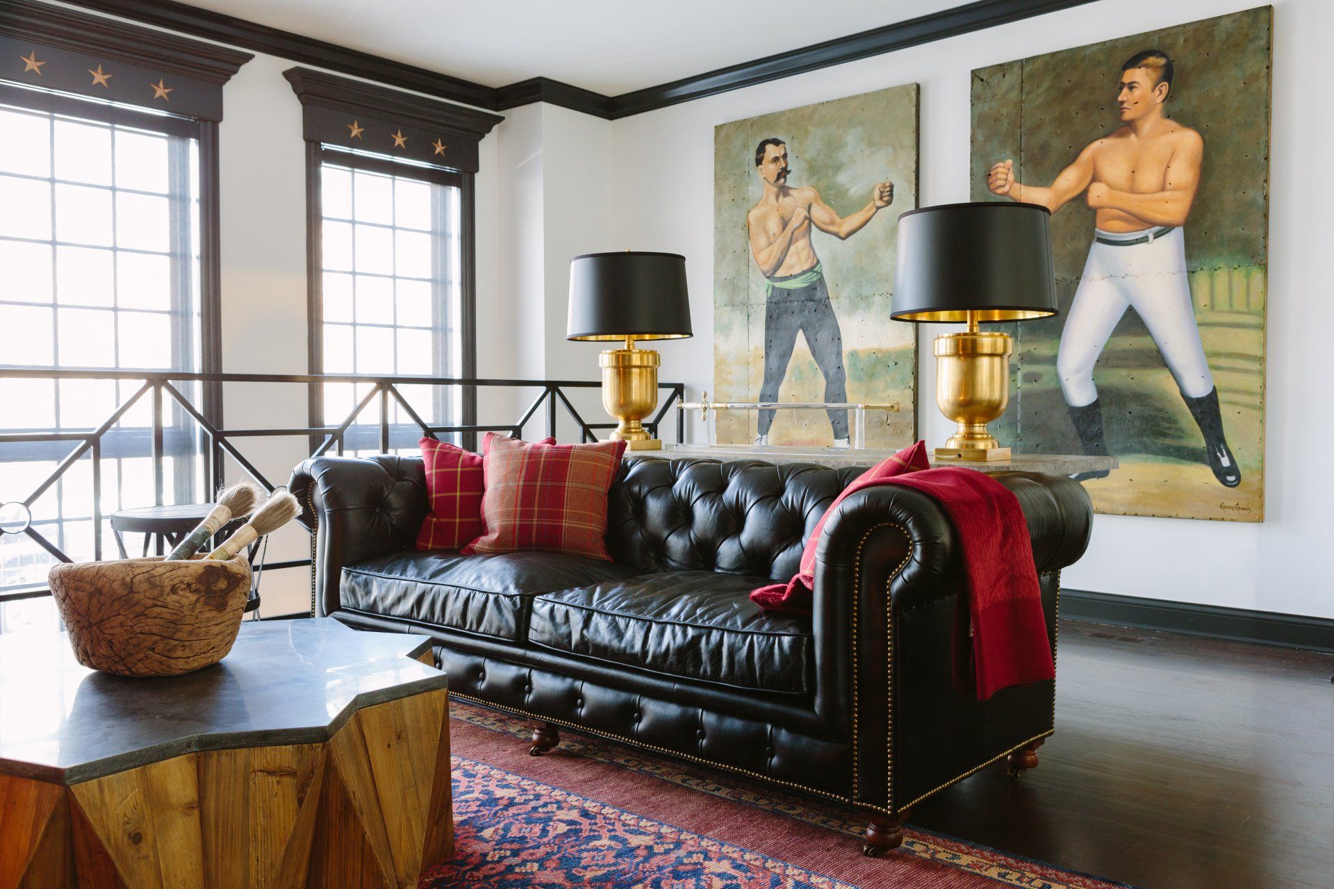 A living room with a black leather couch and two paintings on the wall.