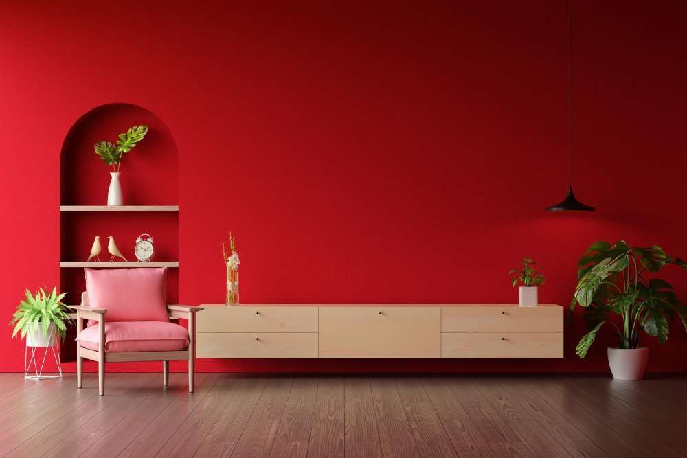 A living room with red walls , a pink chair , a wooden cabinet , and a plant.