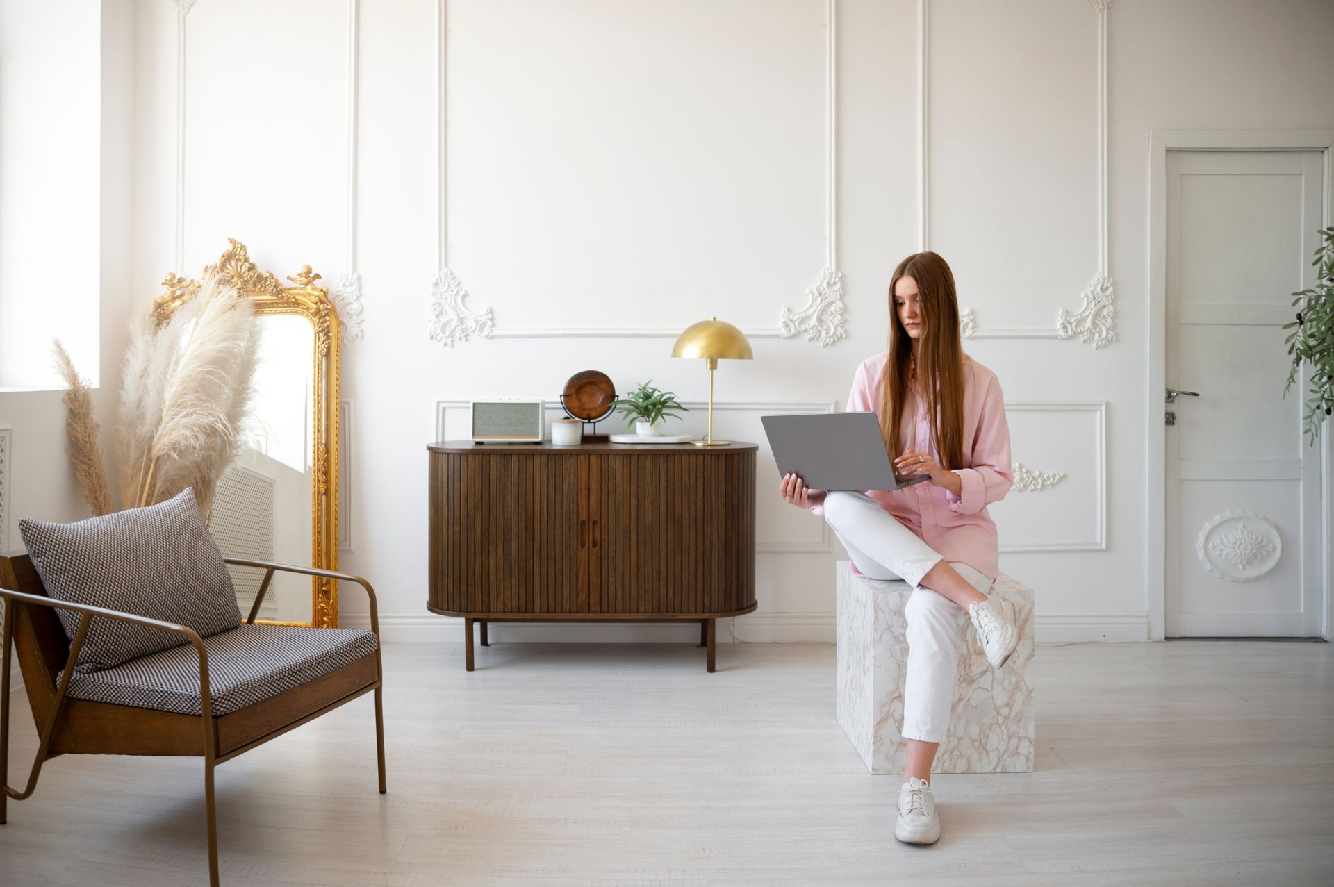 A woman is sitting on a stool in a living room using a laptop computer.