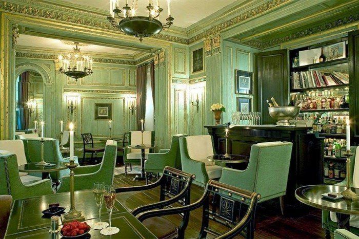 A room with green chairs and tables and a bar.