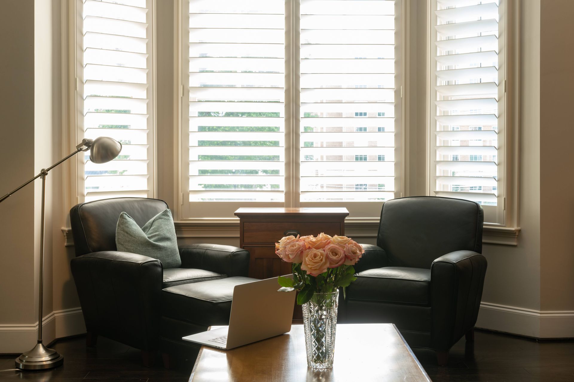 Custom shutters on bay windows in a cozy nook of a home office, featuring two armchairs at Custom Wood Shutters and Blinds near Tustin, CA