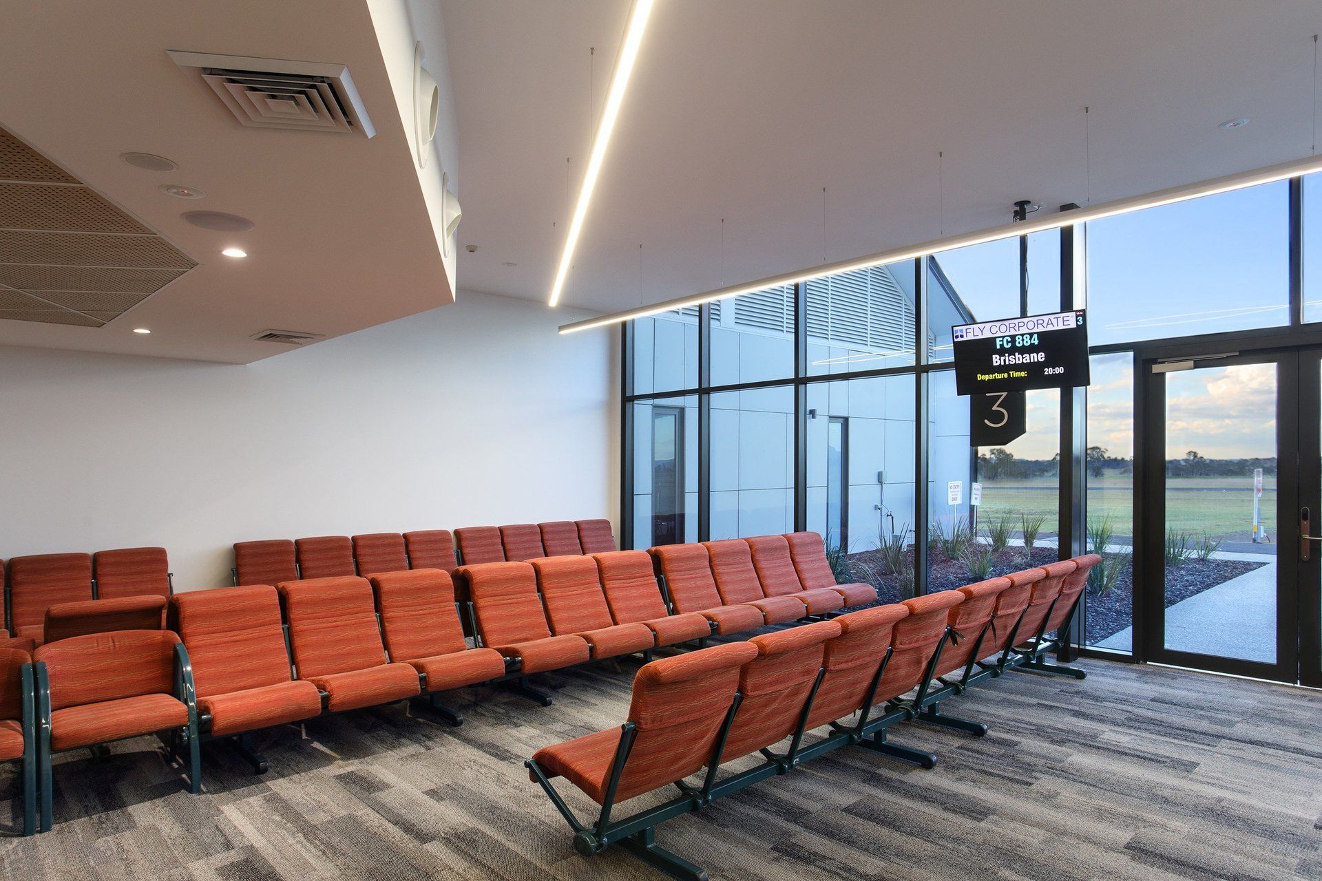 departures area of armidale airport with rows of orange chairs and a large window .