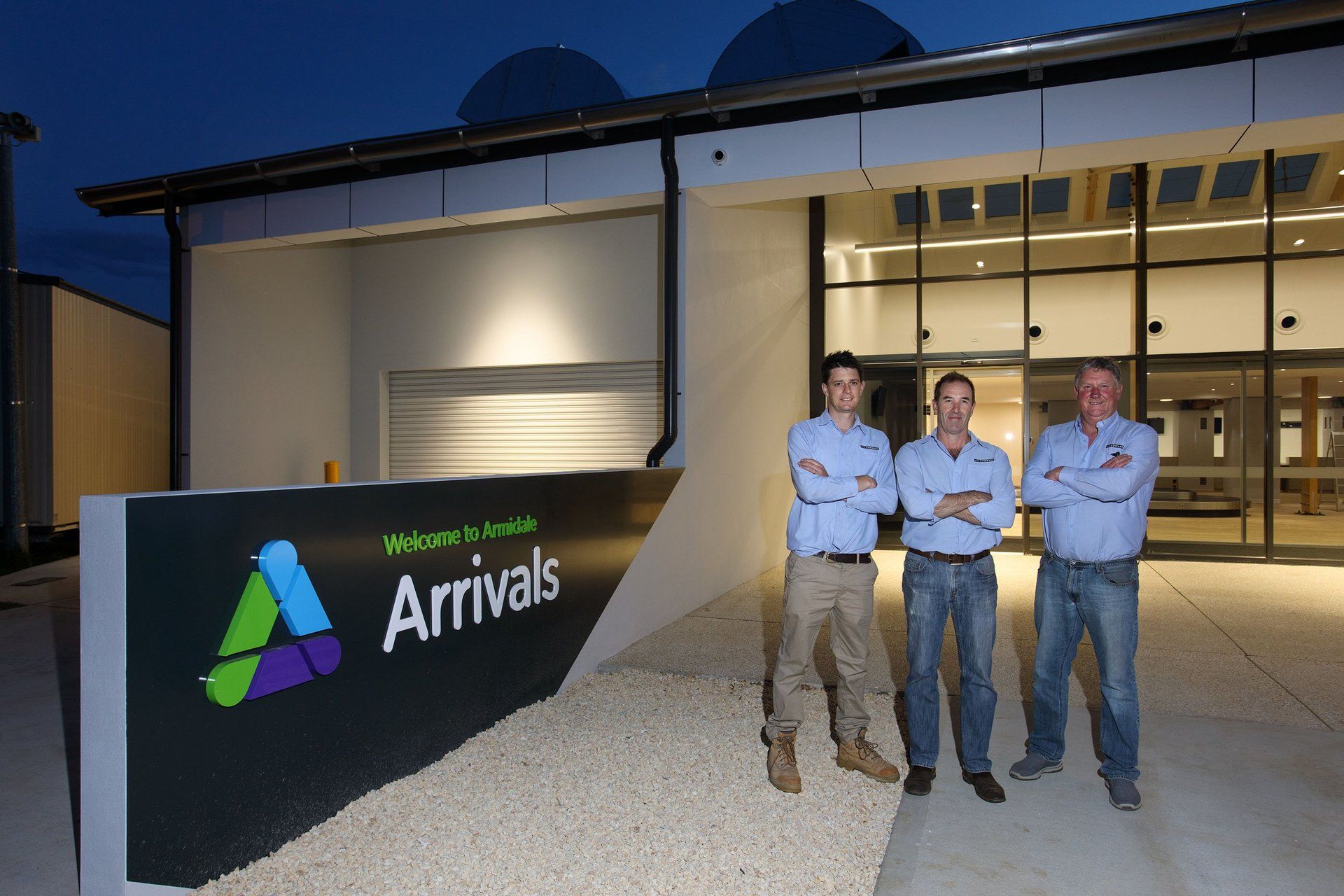 three men standing in front of a sign that says arrivals at armidale airport