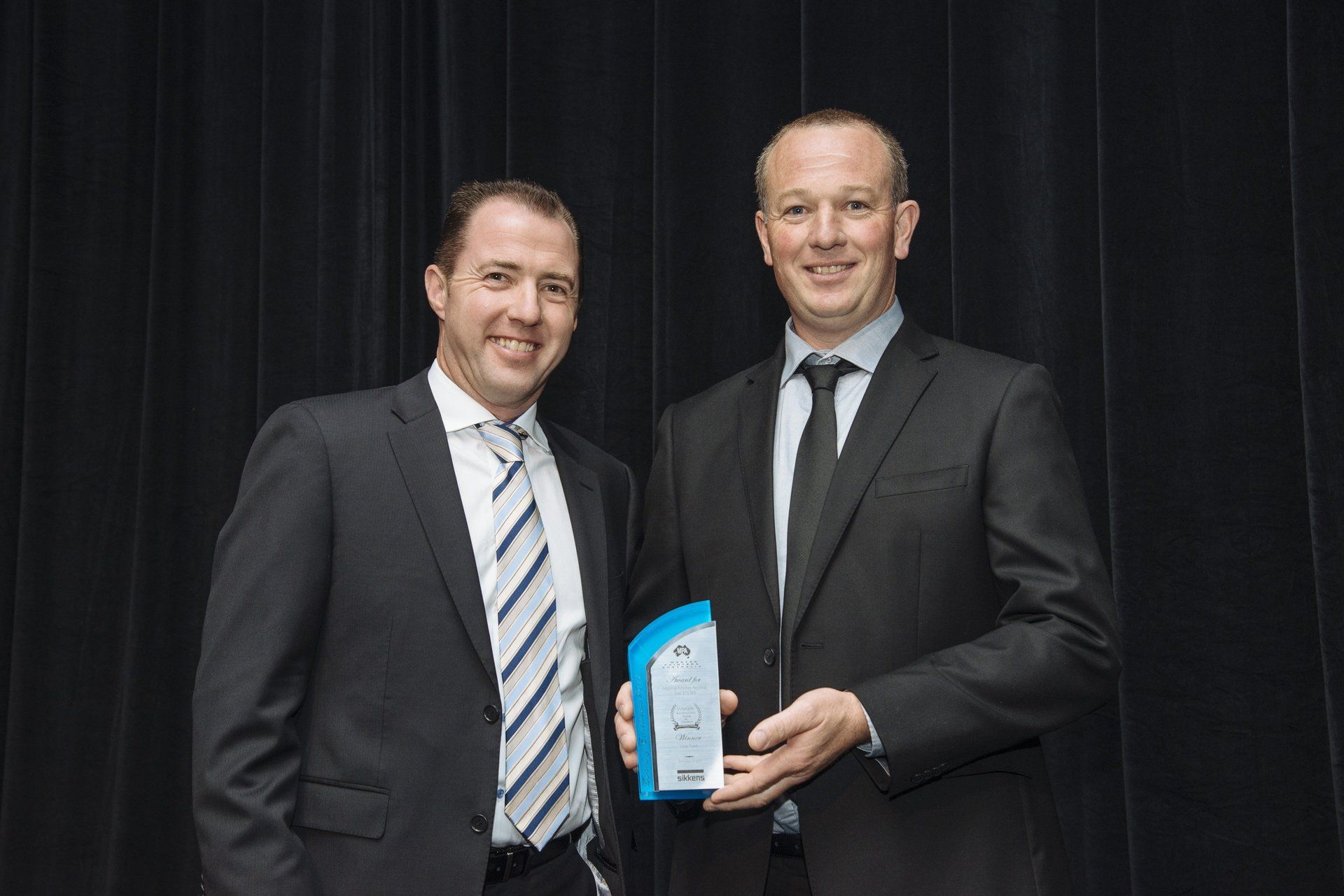 two men in suits and ties are standing next to each other holding an award .