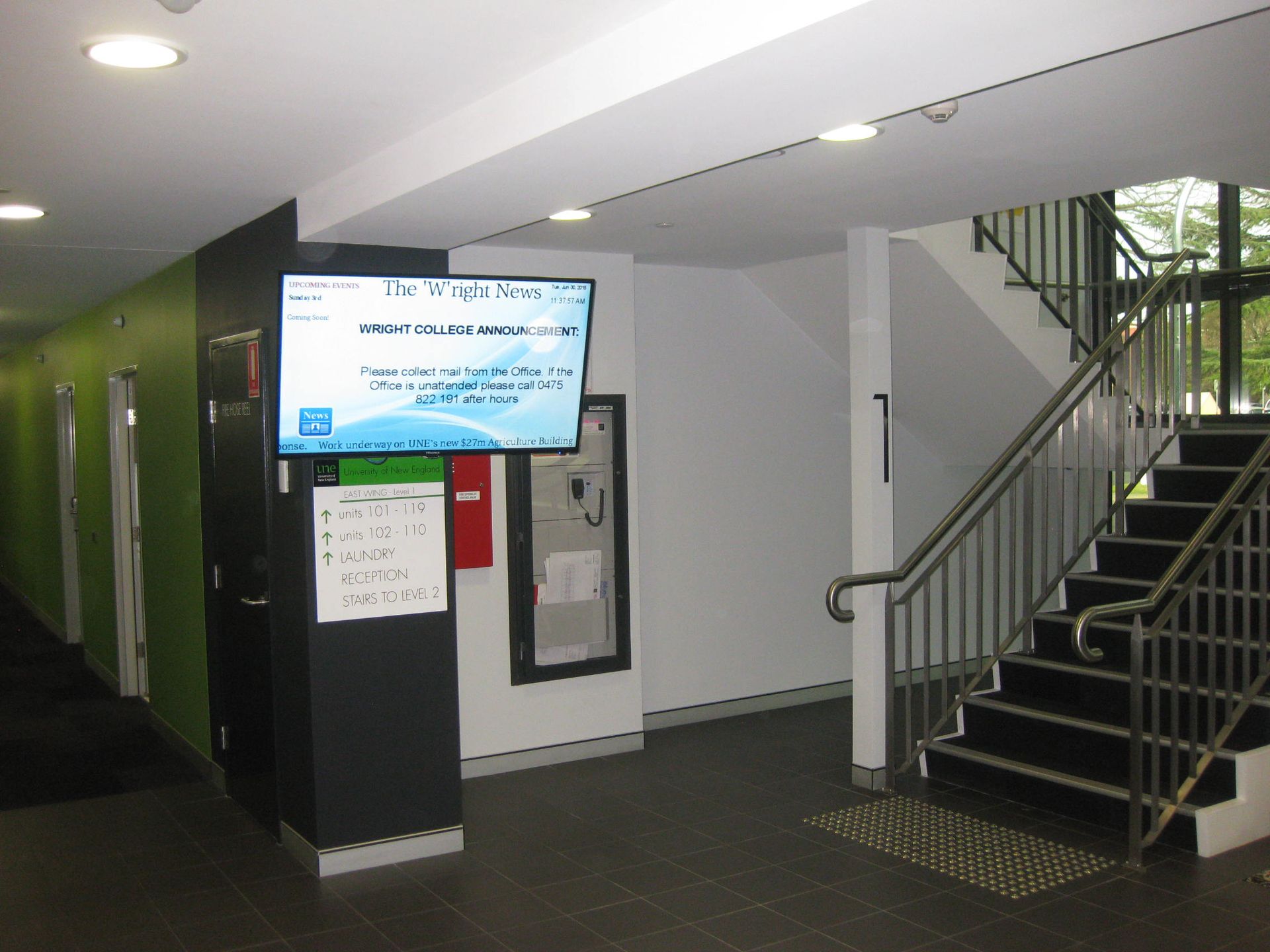 a hallway with stairs and a tv on the wall showing announcements from wright college in armidale
