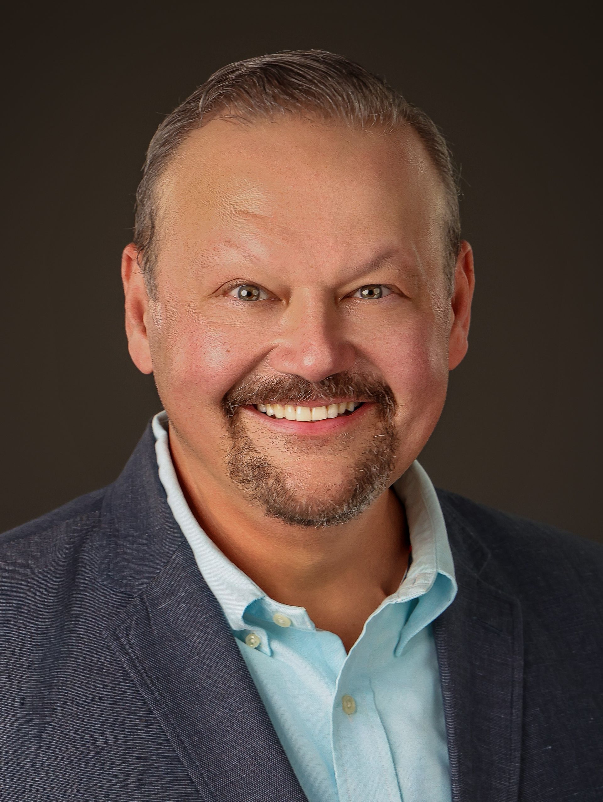 A man with a beard and a blue jacket is smiling for the camera.
