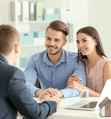 A couple sits at a desk smiling while meeting with a professional in an office setting.